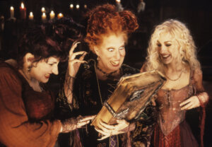 The Sanderson sisters from Hocus Pocus excitedly holding the magical spellbook by candlelight