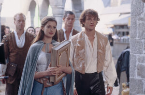 Anne Hathaway and James Frain in medieval costumes walking in a stone archway scene from The Princess Diaries 2