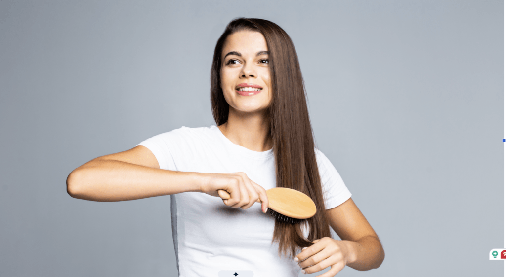 Young woman with long brown hair brushing her hair wearing a white t-shirt against a gray background