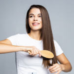 Young woman with long brown hair brushing her hair wearing a white t-shirt against a gray background