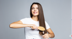 Young woman with long brown hair brushing her hair wearing a white t-shirt against a gray background