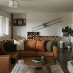 Living room with brown leather sectional sofa, dartboard, foosball table, vintage skis on wall, and white brick fireplace