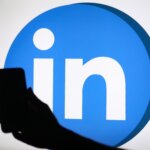 Silhouette of a hand holding a smartphone in front of the LinkedIn logo on a screen