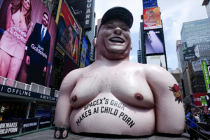 Inflatable caricature of Elon Musk with "SpaceX's Grok Makes AI Child Porn" text in Times Square, New York.