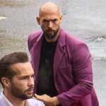 Man in lavender suit adjusting collar with another man in purple blazer and black shirt behind him on wet street