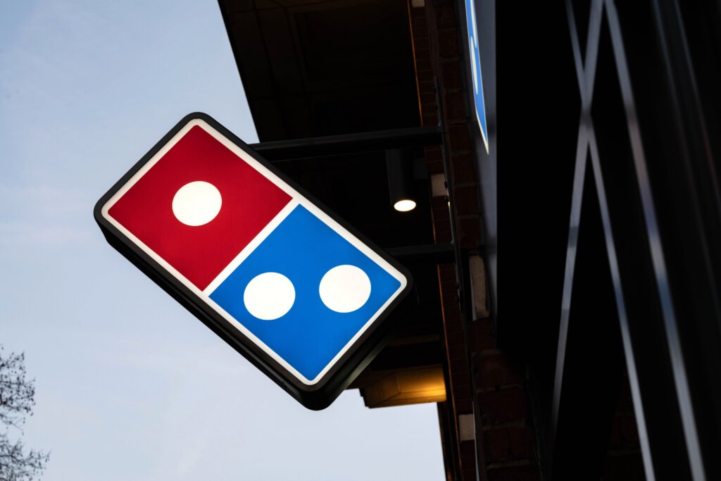 Domino's Pizza illuminated sign mounted on a building exterior at dusk.