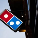 Domino's Pizza illuminated sign mounted on a building exterior at dusk.