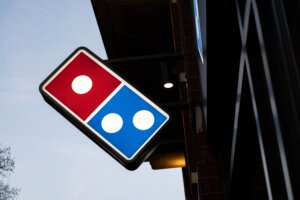 Domino's Pizza illuminated sign mounted on a building exterior at dusk.