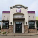 Taco Bell restaurant exterior with purple logo and stone accents under cloudy sky