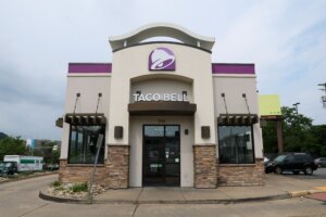 Taco Bell restaurant exterior with purple logo and stone accents under cloudy sky