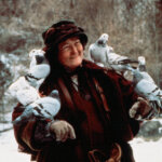 Woman in winter clothing smiling with pigeons perched on her arms and shoulders in a snowy outdoor setting