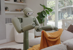 Home robot folding an orange towel in a living room with large windows and plants.