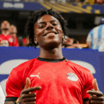 Young man smiling and pointing fingers wearing an Egypt national football team jersey at a stadium event