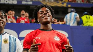 Young man smiling and pointing fingers wearing an Egypt national football team jersey at a stadium event