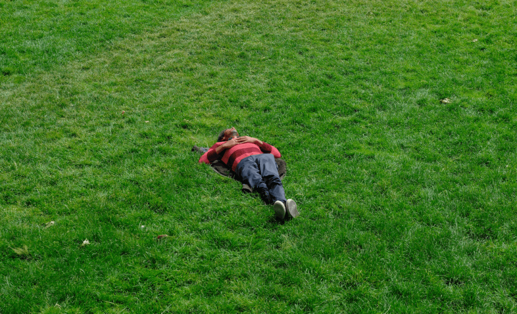 Person lying on green grass wearing a red and black striped sweater and dark pants.
