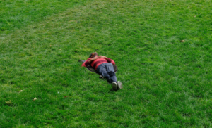 Person lying on green grass wearing a red and black striped sweater and dark pants.