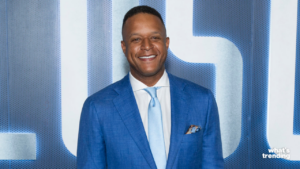 Man in blue suit and light blue tie smiling against a blue and white patterned background