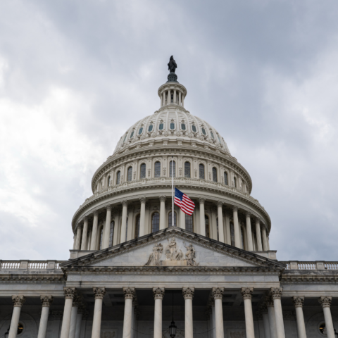 United States Capitol building with American flag flying at half-staff under cloudy sky
