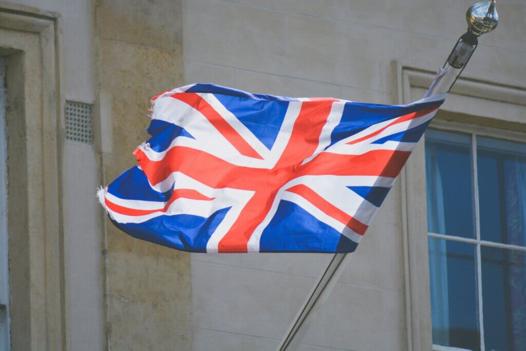 Worn Union Jack flag waving on a pole outside a stone building with windows