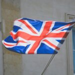 Worn Union Jack flag waving on a pole outside a stone building with windows