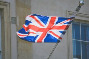 Worn Union Jack flag waving on a pole outside a stone building with windows