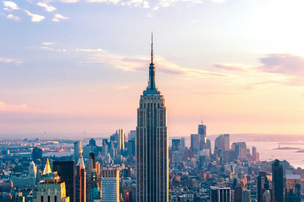 Empire State Building towering over New York City skyline at sunset with pastel sky background