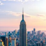 Empire State Building towering over New York City skyline at sunset with pastel sky background