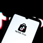 TikTok Shop app logo displayed on a smartphone screen with a blurred TikTok logo in the background