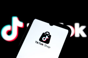 TikTok Shop app logo displayed on a smartphone screen with a blurred TikTok logo in the background