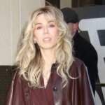Blonde woman wearing a burgundy suit and matching leather coat walking outside a building.