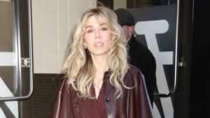 Blonde woman wearing a burgundy suit and matching leather coat walking outside a building.
