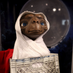 E.T. character wrapped in a white blanket sitting in a crate with a moon backdrop.