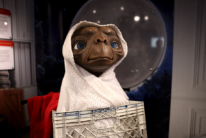 E.T. character wrapped in a white blanket sitting in a crate with a moon backdrop.