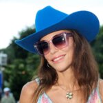 Woman wearing a blue cowboy hat, large sunglasses, and a colorful crochet dress at an outdoor event