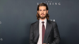 Andrew Garfield in a dark pinstripe suit with a maroon tie at The Uprising event backdrop