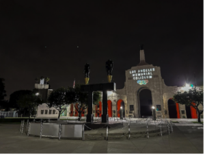 Los Angeles Memorial Coliseum entrance at night with illuminated signage and statues.
