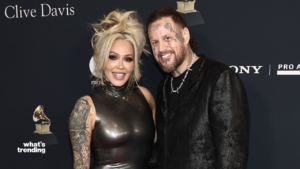 Couple posing on red carpet with tattoos, woman in black latex dress and man in black textured jacket at Clive Davis event