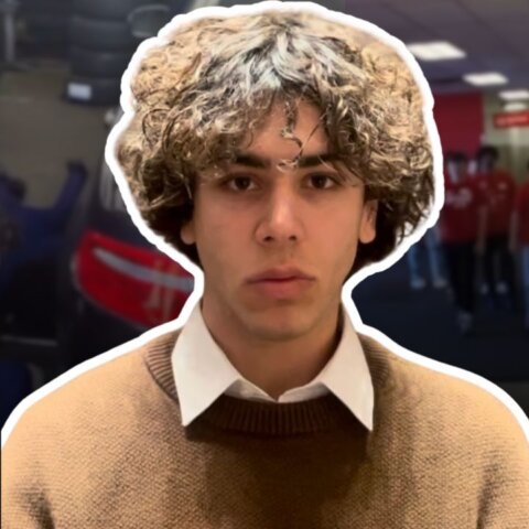 Young man with curly hair wearing a brown sweater and white collared shirt, "what's trending" logo in corner