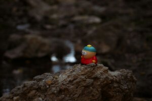 Eric Cartman figurine from South Park on a rock with blurred natural background